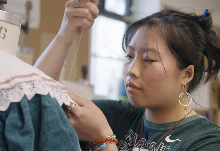 Student Kathrin Poon sews a ruffled color onto a green dress